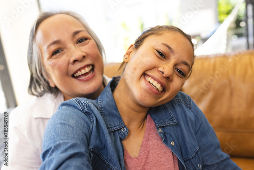 Asian grandmother and biracial teenage granddaughter are smiling together at home
