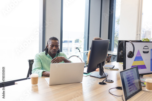 African American man with braided hair working on a laptop in a modern business office