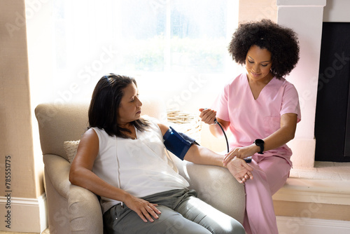 Mature biracial woman getting blood pressure checked by young biracial nurse at home