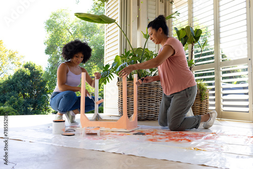 Biracial mother and adult daughter are painting furniture outside at home for an upcycling project