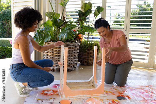 Biracial mother and adult daughter painting furniture together at home in an upcycling project