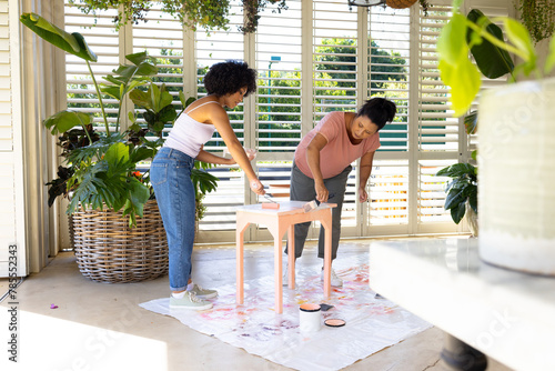 Biracial mother and adult daughter are painting a stool together at home as an upcycling project
