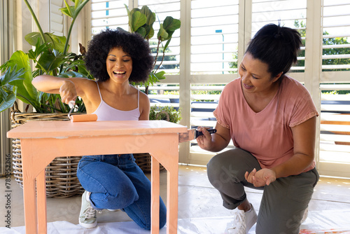 Biracial mother and adult daughter painting furniture together at home in an upcycling project
