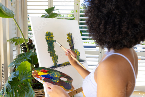Biracial young woman painting on canvas at home, focusing intently