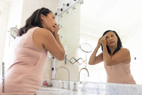 Mature biracial woman removing makeup in the bathroom, looking in mirror at home