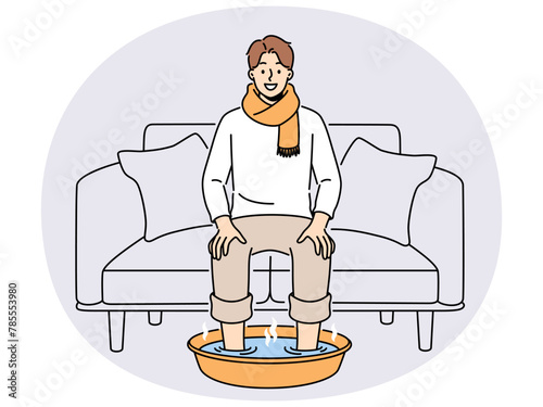 Smiling man in scarf sit on sofa at home soak feet in hot water. Happy male suffer from cold or flu do procedures for fast recovery. Healthcare. Vector illustration.