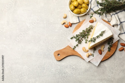 Piece of tasty camembert cheese, thyme, nuts and olives on grey textured table, flat lay. Space for text