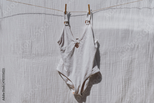 Bikini swimsuit hanging on rope over white cloth with strong shadows. Sunny day sunbathing. Chic fashion