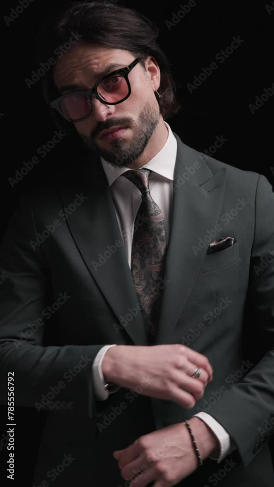 cool bearded businessman with sunglasses looking to side, adjusting suit, crossing arms and being cool with hands in pockets on black background cool bearded businessman with sunglasses looking to side, adjusting suit, crossing arms and being cool with hands in pockets on black background