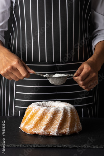 Woman powder of sugar to vanilla bundt cake on dark background. photo