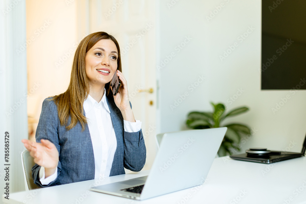 Professional woman engages in an animated conversation over the phone at her bright office desk Professional woman engages in an animated conversation over the phone at her bright office desk