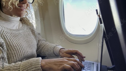 One adult woman travel on airplane on board using laptop computer sitting on the seat near thw window. Traveler on aircraft. Flight business online with computer. Modern traveler working and fly photo