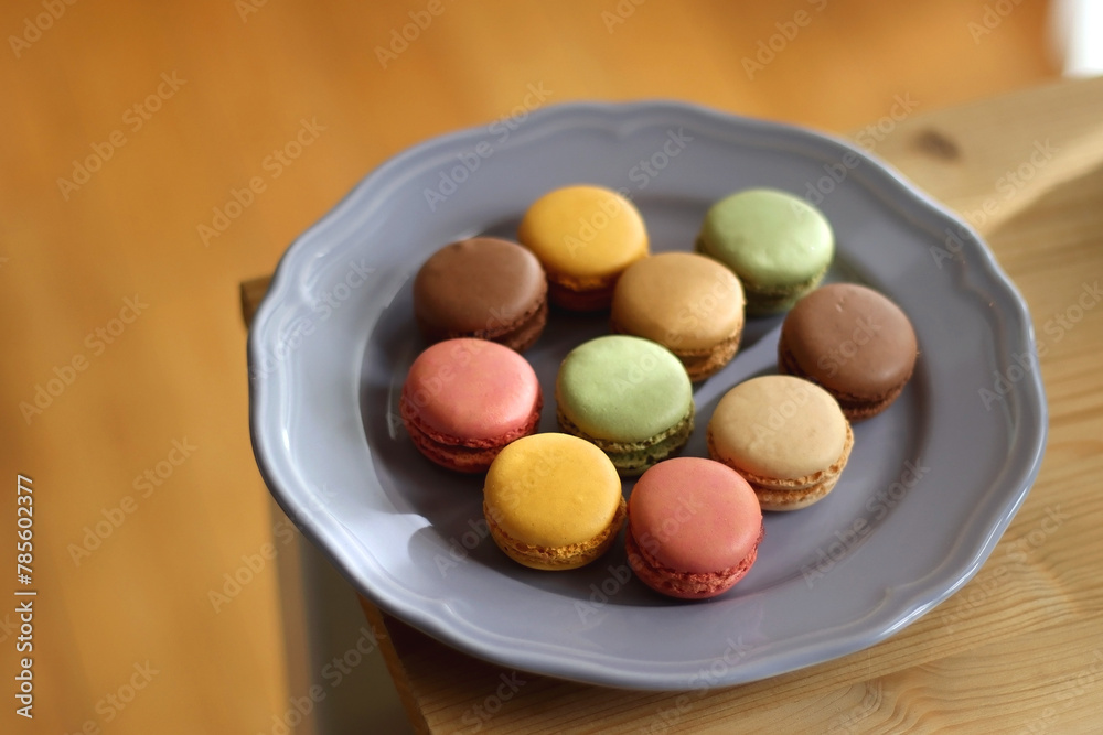 Purple plate filled with pastel macarons on wooden table. Selective focus. Purple plate filled with pastel macarons on wooden table. Selective focus.