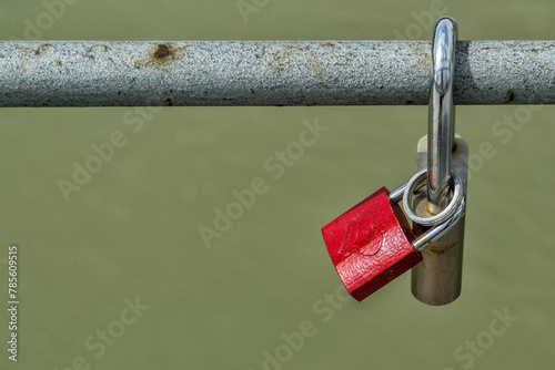 A red padlock with a heart hanging from a metal bar on a bridge
