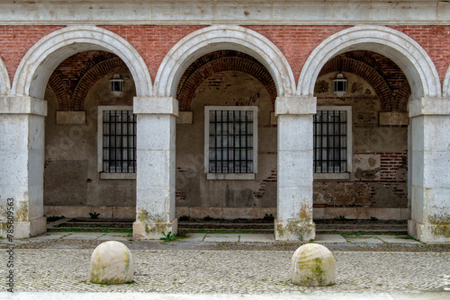 Three neoclassical style arches with windows and two bollards in front in one of the galleries on a street in Aranjuez, province of Madrid. Spain