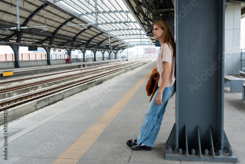 Woman leaning against column at empty train station platform. Urban commuting concept with copy space for design and print.