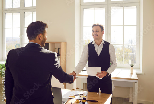 Business people shaking hands at end of meeting. Smiling lawyer and his client shake hands after successful legal consultation. Two men in business suits are concluding contract in office. photo