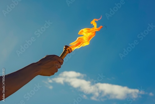 A mans hand raises the burning Olympic flame against a blue sky