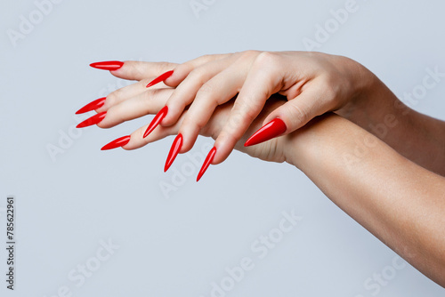 Foto Closeup of  elegant female hands with red stiletto nails on gray background