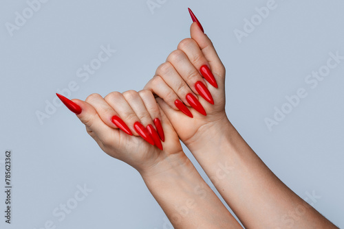Closeup of elegant female hands with red stiletto nails on gray background