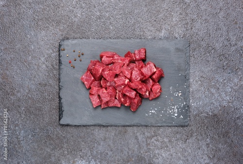 Sliced raw beef meat for slices for the preparation of goulash, stew on a shaleboard on a black concrete background.