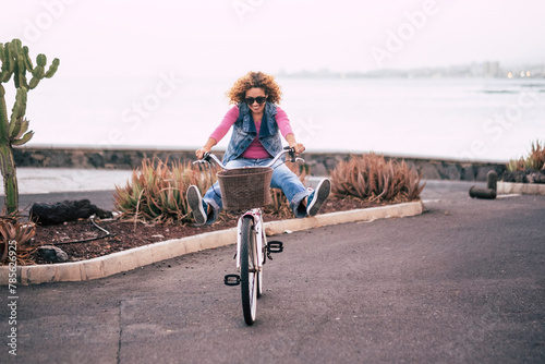 A curly woman with blonde hair and sunglasses have fun riding a bike in outdoor leisure activity happily playing and having fun on her bicycle on the street. Tourist has fun on vacation