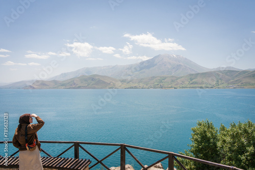 Veiled Muslim woman enjoying views on beautiful lake with mountains in backdrop, Turkey
