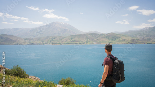 Young athletic man with backpack enjoying views on beautiful lake with mountains in backdrop, Turkey