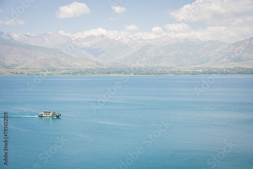Sightseeing boat with tourists sailing on beautiful blueish lake with mountains in backdrop, Turkey