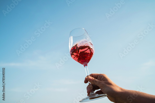 Female hand delicately holds a glass of rose wine against blue clear sky