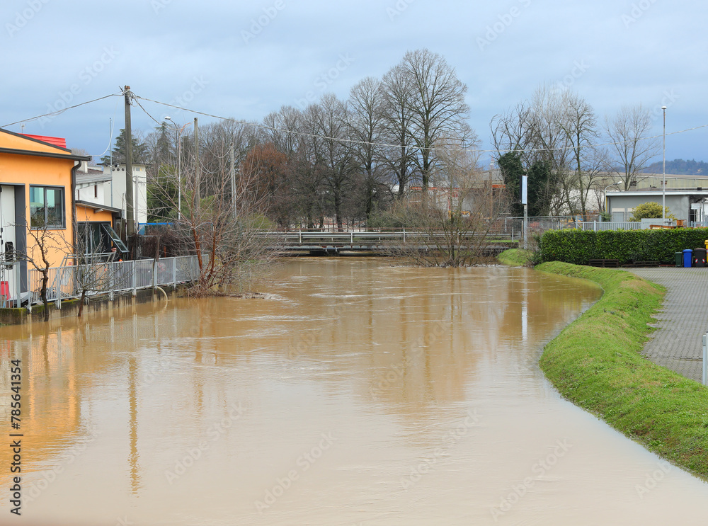 Fototapeta premium Swollen river flooded after the flood in the industrial area with warehouses at risk of flooding