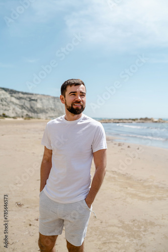 Man wearing a white t-shirt walks along the beach, enjoying the serenity of the seaside during his holiday