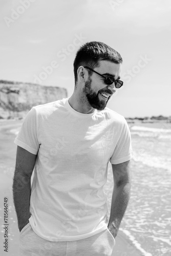 Man wearing a white t-shirt walks along the beach, enjoying the serenity of the seaside during his holiday