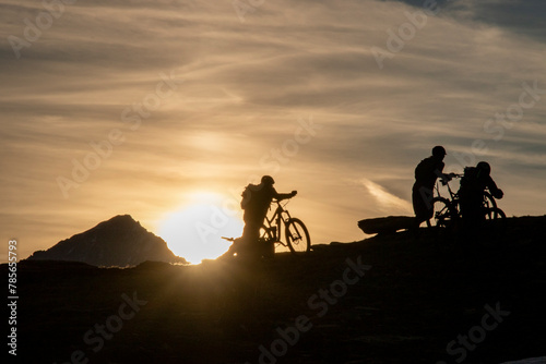 Silhouetted cyclists at sunset on a summer mountain trail photo