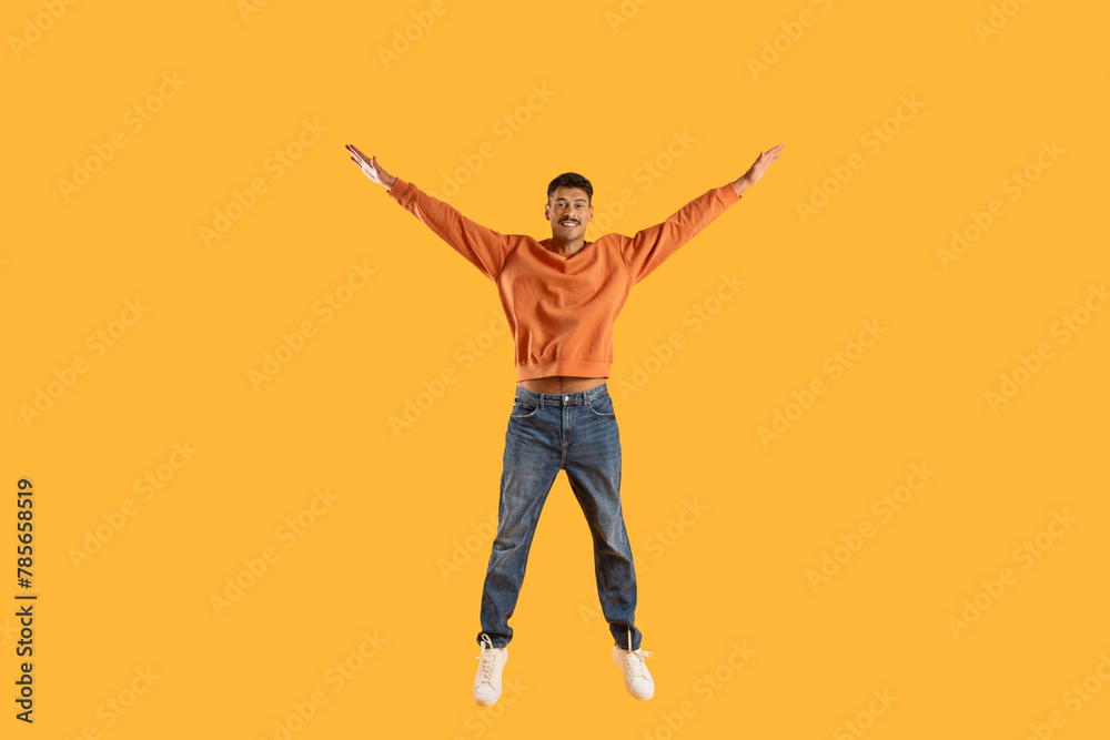 Excited man jumping with joy against yellow background