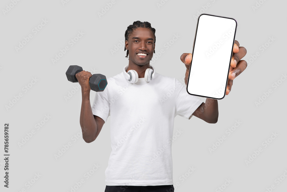 Smiling man showing smartphone and holding dumbbell Smiling man showing smartphone and holding dumbbell