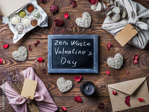 Zero waste Valentine's Day concept. Eco-friendly gift cloth wrapping in Furoshiki style, homemade sweets as gift ideas and chalkboard with Zero Waste Valentine's Day letters on brown wooden background