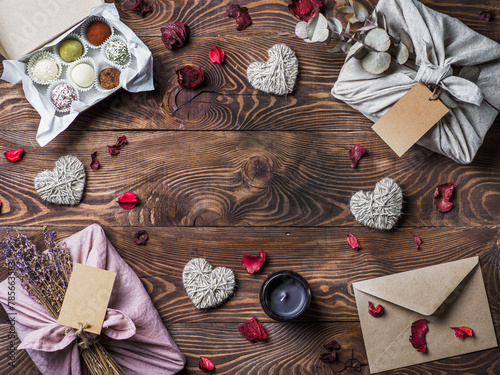 Zero waste Valentine's Day concept. Eco-friendly gift cloth wrapping in Furoshiki style, homemade sweets and candle as gift ideas on brown wooden background. Copy space in center