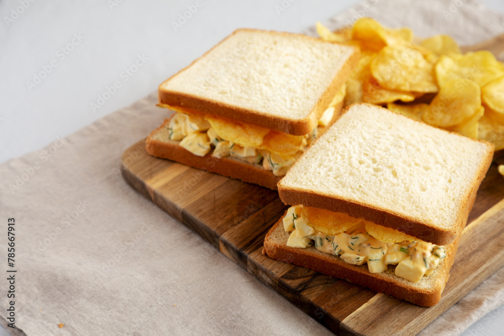 Homemade Egg Salad Sandwich with Potato Chips on a wooden board, side view. Copy space.
