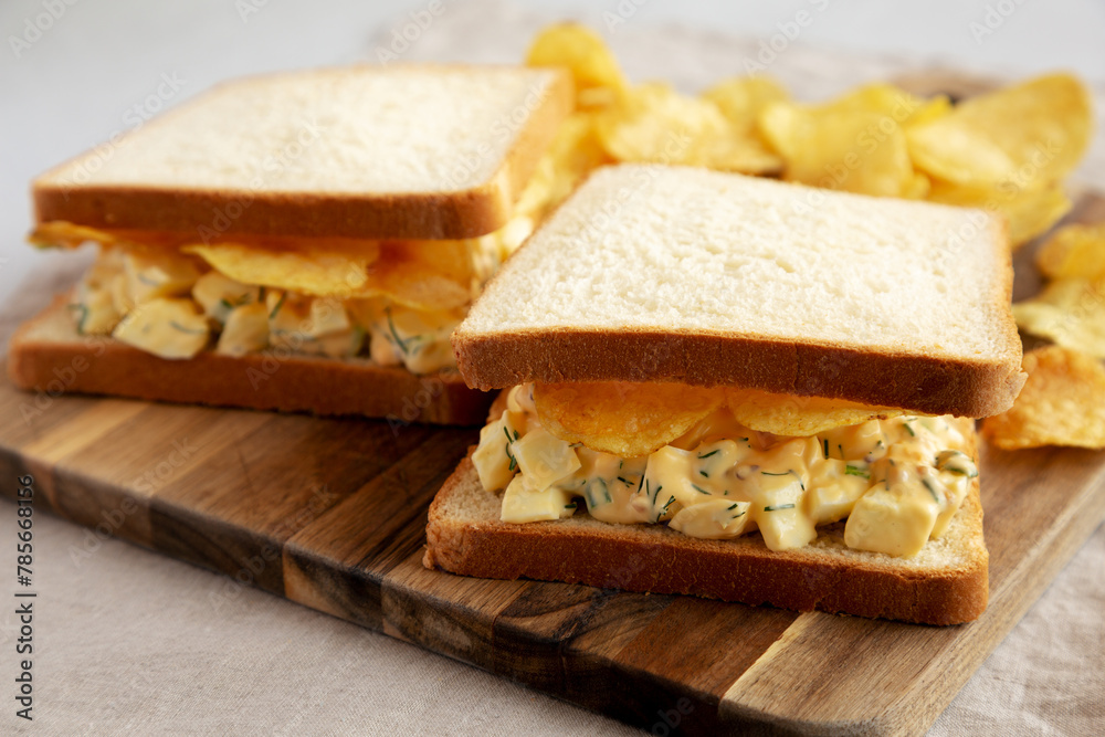 Homemade Egg Salad Sandwich with Potato Chips on a wooden board, side view. Close-up.