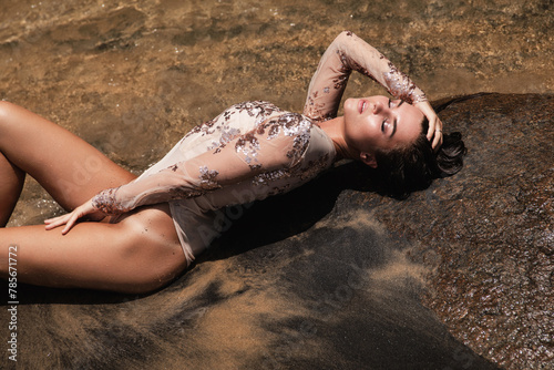 Gorgeous young woman wearing sequin bodysuit lying on the beach