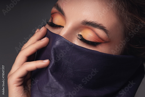 Portrait of a woman with striking eye makeup and leather wild rag covering her face