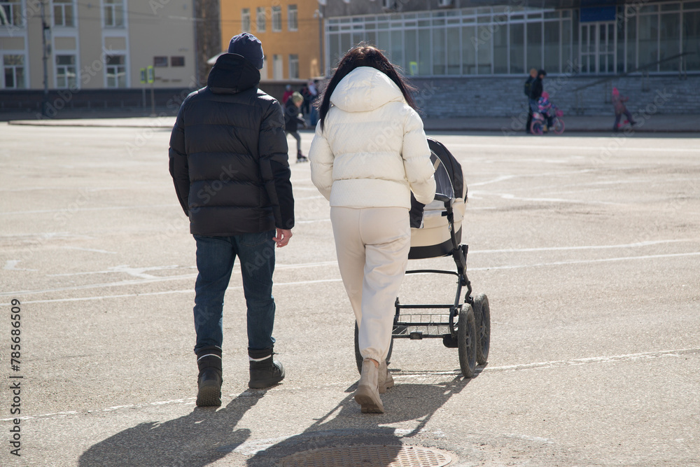  a woman and a man walk with a stroller containing a small child.