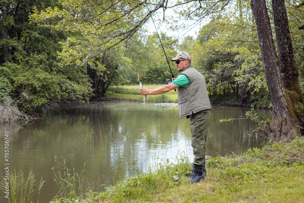 Young fisherman fishing on the river bank surrounded by beautiful green nature, using small fish as bait on the hook. Sport and recreation concepts. Young fisherman fishing on the river bank surrounded by beautiful green nature, using small fish as bait on the hook. Sport and recreation concepts.