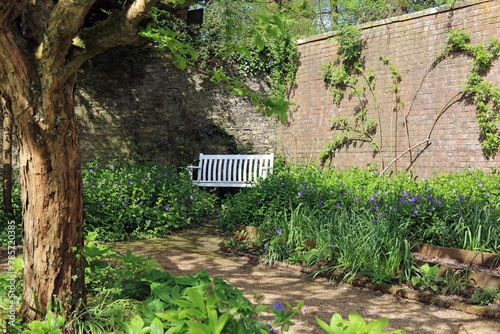 A white wooden bench seat in the corner of a walled garden