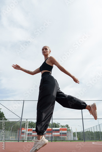 An exuberant female athlete jumps with open arms against a blue sky, showcasing freedom, fitness, and the joy of exercise.