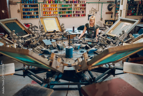 Female graphic worker operating screen carousel printing press at factory