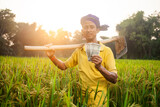rural farm worker showing indian paper currency and holding a garden hoe on his shoulder standing in his field