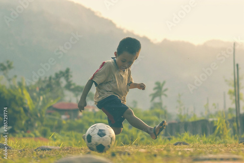 Young Boy Kicking Soccer Ball in Rustic Field at Sunset © kegfire