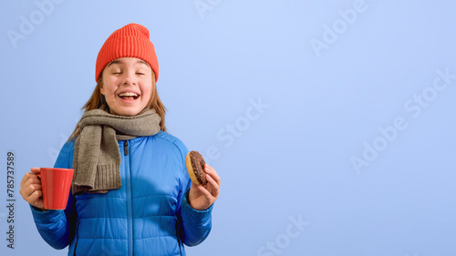 Laughing young girl 10-12 years old holding a donut and a cup of tea. on a blue background © KiNOVO